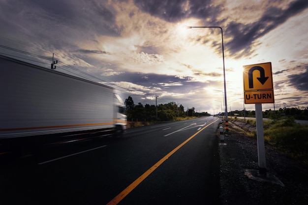 Verschwommene Container-LKW-Fahrt durch U-Turn-Schild während des Sonnenuntergangs auf der Landstraße.