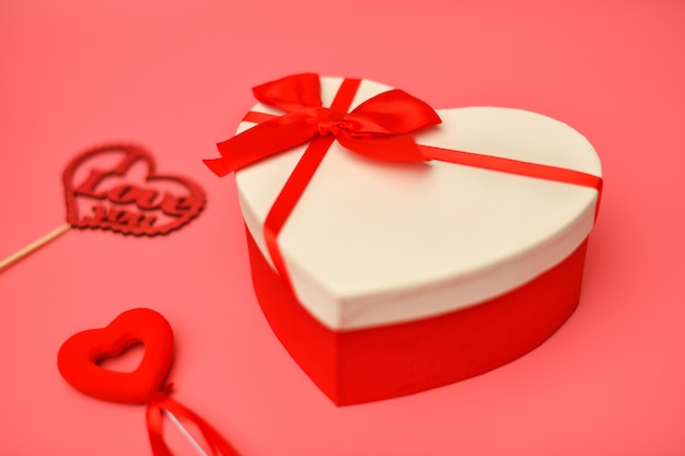 Verschwommene Geschenkbox zum Valentinstag herzförmig mit einem roten Band auf einem Rosa