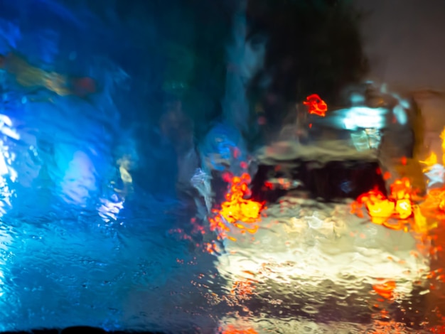 Verschwommene Regentropfen auf Autofenster mit Straßenlicht-Bokeh auf abstraktem Hintergrund der Regenzeit