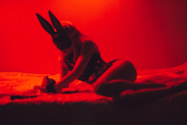 Verschwommene Silhouette eines sexy devoten Mädchens in Unterwäsche und einer Maske liegt auf dem Bett im Schlafzimmer BDSM-Konzept von Sex