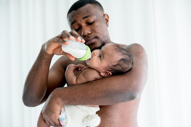 Verschwommene Weichheit des afrikanischen Vaters, der seiner neugeborenen Tochter Milch aus der Flasche füttert