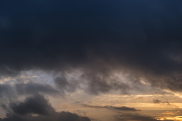 Verschwommener dunkler Himmelshintergrund mit flauschigen, lockigen, rollenden Wolken am Abend mit untergehender Sonne Gutes windiges Wetter