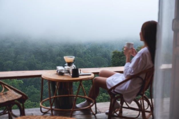 Verschwommenes Bild einer Frau, die Tropfkaffee trinkt und an einem nebligen Tag einen wunderschönen Blick auf die Natur betrachtet