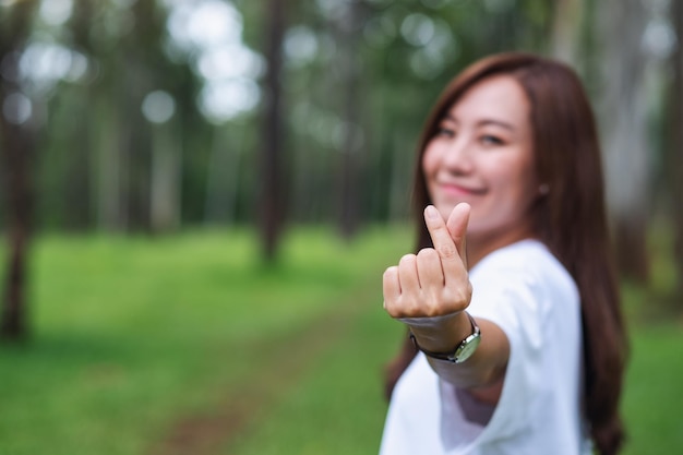 Verschwommenes Bild einer schönen asiatischen Frau, die im Park ein Mini-Herz-Handzeichen macht