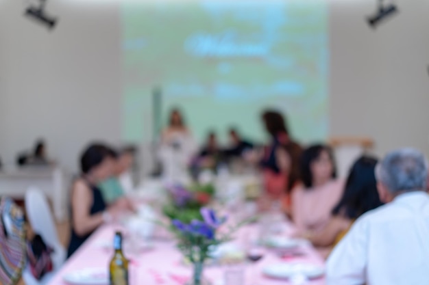 Verschwommenes Essen mit Projektor und weißer Leinwand für das asiatische Publikum, das an der langen Tischreihe sitzt