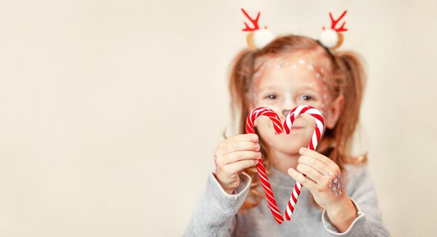 verschwommenes Mädchen in Weihnachtshörnern faltete Lutscher in Form eines Herzens