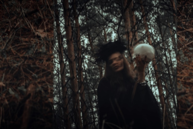 Verschwommenes mystisches Spiegelbild im Spiegel einer bösen, beängstigenden Hexe mit dem Schädel eines Toten, der mystische okkulte Rituale im Wald heraufbeschwört