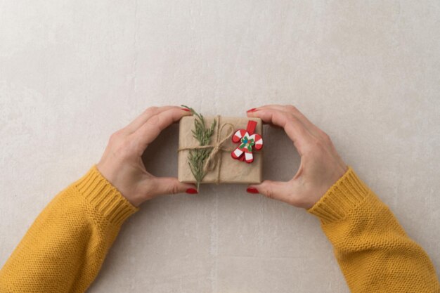 Verschwommenes Weihnachtsgeschenk in weiblichen Händen in einer gelben Jacke, Draufsicht, heller Betonhintergrund