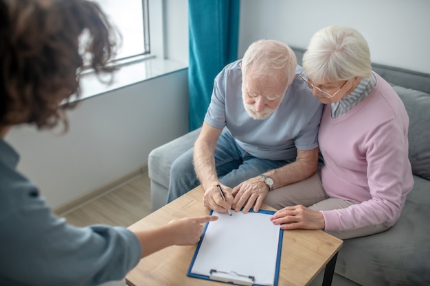 Versicherung. Älteres Paar, das einen Termin mit dem Krankenversicherungsagenten hat und den Vertrag unterzeichnet