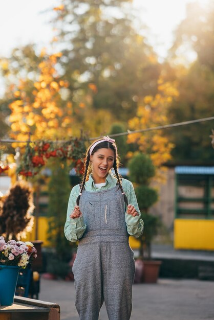 Verspielte Bäuerin in Denim-Overalls, die aufrichtig lächelt, während sie posiert