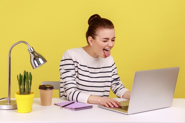 Verspielte Büroangestellte in gestreiftem Hemd, die die Zunge heraus zeigt und positive kindliche Emotionen ausdrückt