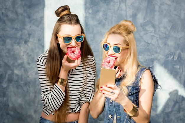 Verspielte Frauen, die Spaß mit süßen Donuts auf dem blauen Wandhintergrund haben