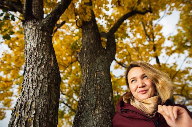 Verspielte junge Frau, die die gelben Blätter des Herbstes im Herbstpark genießt, fühlt saisonale Daten