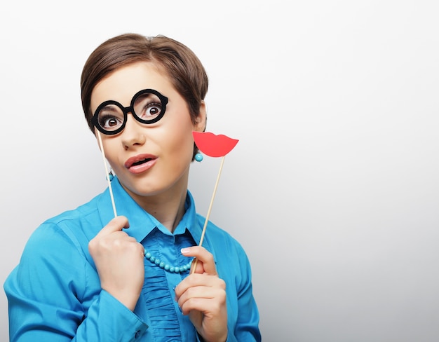 verspielte junge Frau, die Lippen und Brille auf einem Stock hält