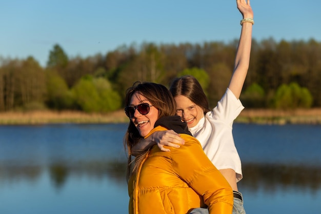 Verspielte Mutter, die Tochter huckepack am Ufer des Frühlingssees reitet