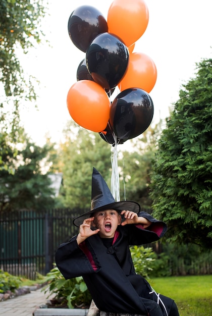 Verspielter kleiner Junge im Karnevalskostüm des Zauberers droht Halloween im Hinterhof zu feiern