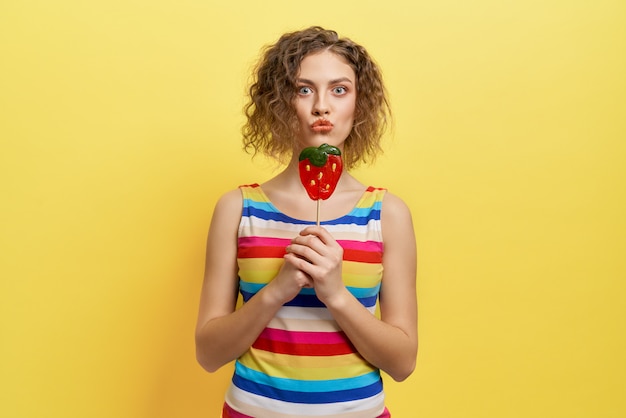 Verspieltes Mädchen im gestreiften Kleid, das Beerenlutscher hält.