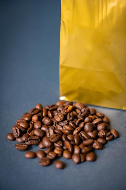 Verspotten Sie goldene metallische Papierbeuteltasche auf einem blauen Hintergrund, der an Kaffeebohnen mit Zimt liegt