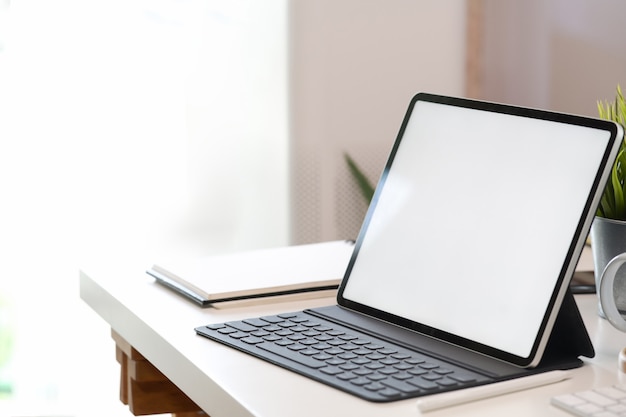 Verspotten Sie herauf Tablette des leeren Bildschirms mit intelligenter Tastatur auf weißem Schreibtisch
