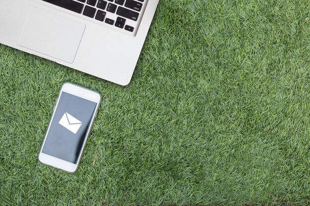 Verspotten Sie Laptop und intelligentes Telefon auf künstlichem grünem Gras mit eMail-Alarm auf Schirm