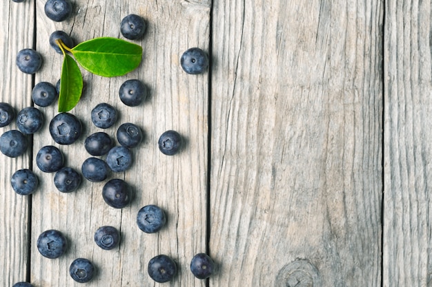 Verstreute Bio-Blaubeeren mit Blättern auf Holzuntergrund