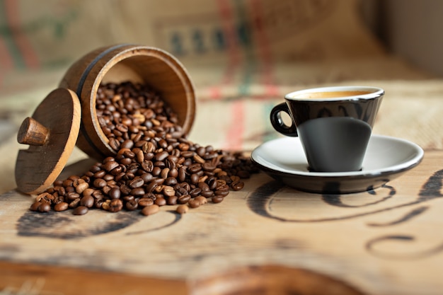 Verstreute Kaffeebohnen, eine Tasse Espresso, Schokoladenstücke mit Nüssen auf einem Holzbrett.