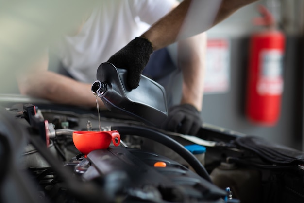 Verter aceite en el motor del coche. Cierre el trabajo manual mecánico masculino y el servicio en la estación de servicio de automóviles