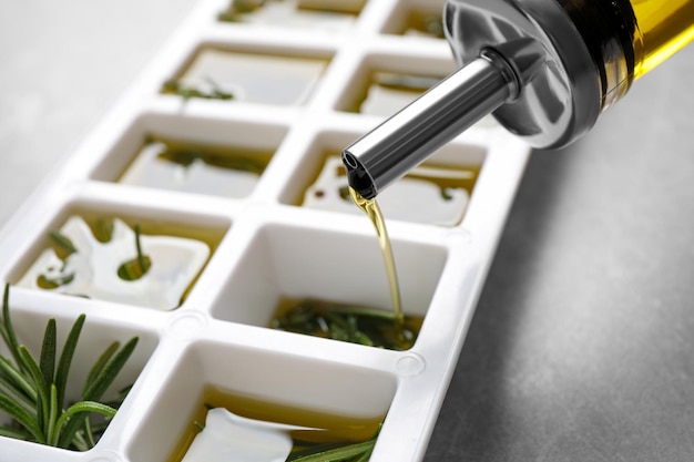 Foto verter aceite de oliva en una bandeja de cubitos de hielo con romero fresco en el primer plano de la mesa gris