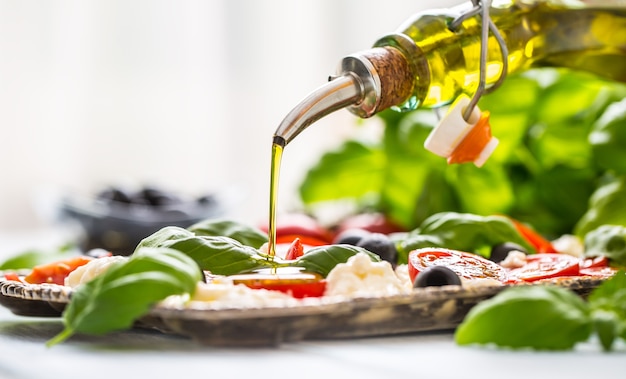 Verter aceite de oliva en ensalada caprese. Comida italiana o mediterránea saludable