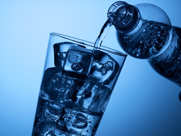 Foto verter agua de una botella de plástico en un vaso con hielo sobre un fondo azul claro