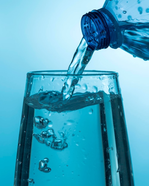Verter agua de una botella de plástico en un vaso de precipitados sobre un fondo azul.