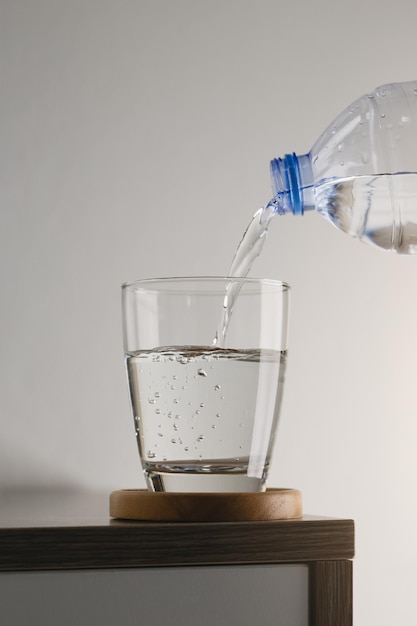 Verter agua de una botella de plástico en vidrio sobre una mesa de madera