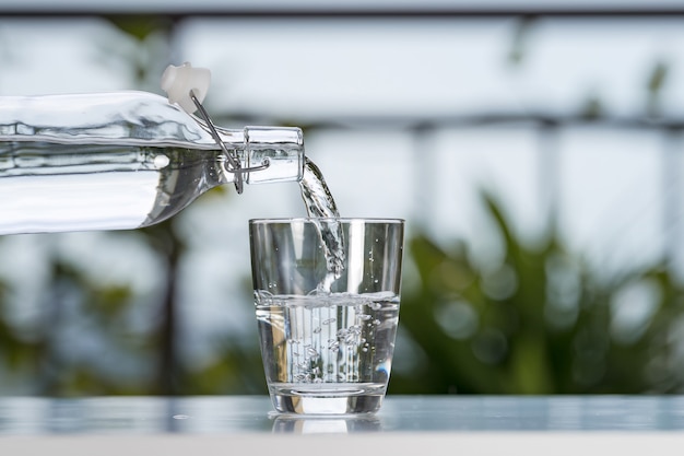 Verter el agua de la botella en un vaso en la casa del jardín