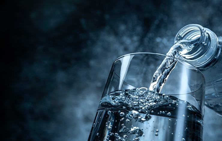 Foto verter el agua de la botella en vidrio om fondo de textura negra con espacio de copia