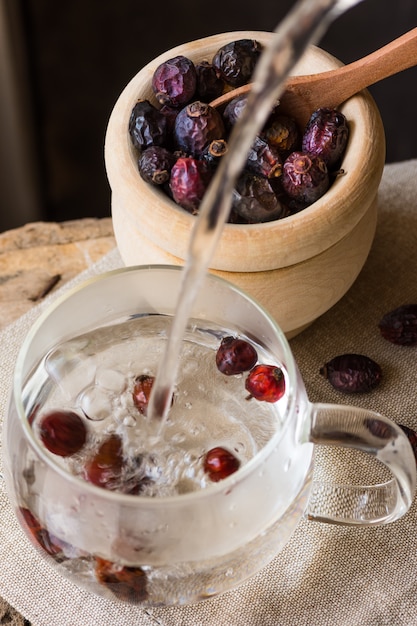 Verter agua caliente en una taza de vidrio que prepara té de rosa mosqueta de bayas