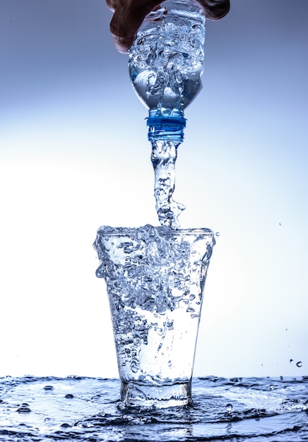 Foto verter agua y chapotear en el vaso con reflejo en el espejo.