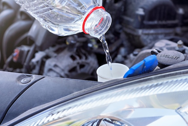 Verter agua destilada (alternativa ecológica al líquido de lavado) al tanque de lavado en el automóvil, detalle en una botella de plástico transparente