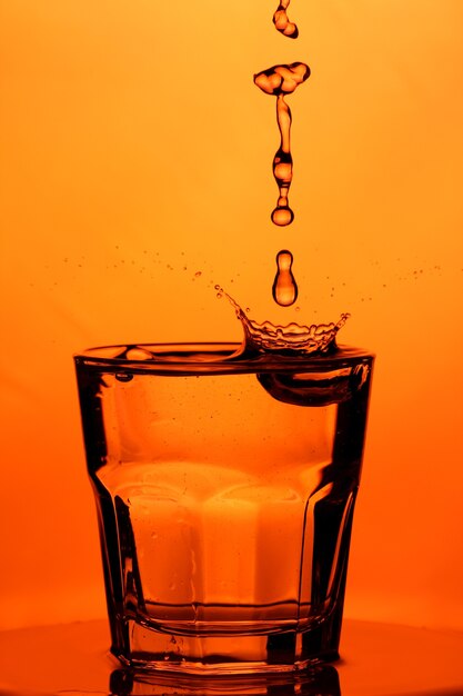 Verter agua en un vaso. Salpicaduras de agua en un vaso sobre fondo naranja