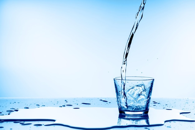 Foto verter agua en un vaso sobre fondo azul.