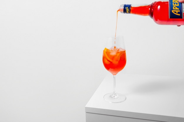 Verter el aperol en copa de vino con hielo sobre fondo blanco.