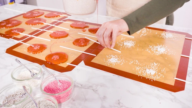 Verter azúcar caramelizada sobre tapetes de silicona para hacer piruletas caseras.
