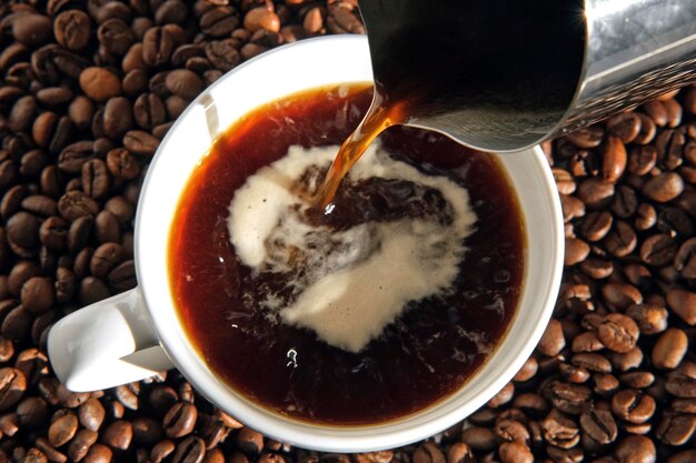 Verter café negro en una taza de cerámica blanca Vista superior Cerrar Bebida de café caliente verter en una taza de una cafetera moka brillante Fondo de granos de café tostados Espresso americano recién hecho