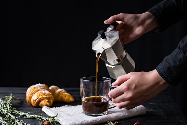 Foto verter el café de un percolador italiano, tiro en clave baja. manos masculinas vierten café negro de cervecero moka italiano