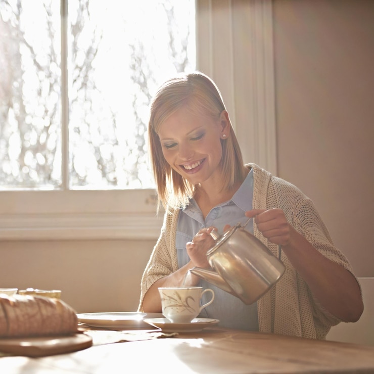 Foto verter chá e mulher feliz em casa para a manhã rotina calma e beber na mesa menina relaxar e pausa para café com lanches de comida ou chaleira nas mãos para a preparação do pequeno-almoço em férias ou férias