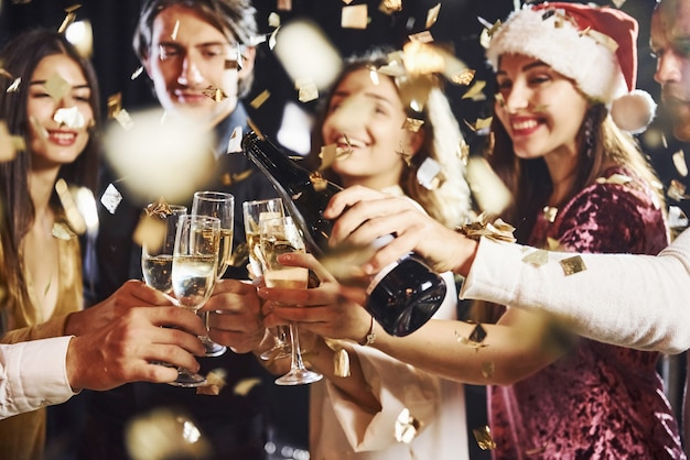 Verter champán. Grupo de amigos alegres celebrando el año nuevo en el interior con bebidas en las manos.