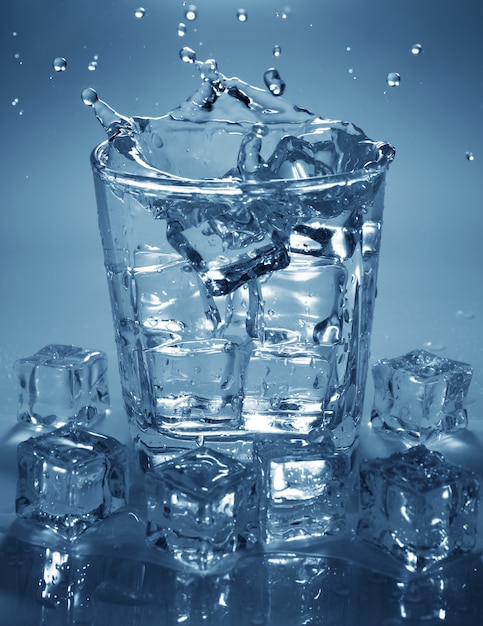 Verter el cubo de hielo en un vaso de agua de bebida. Salpicaduras de agua.