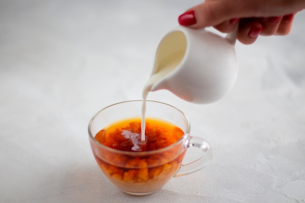 Foto verter la leche de la jarra en una taza de té negro