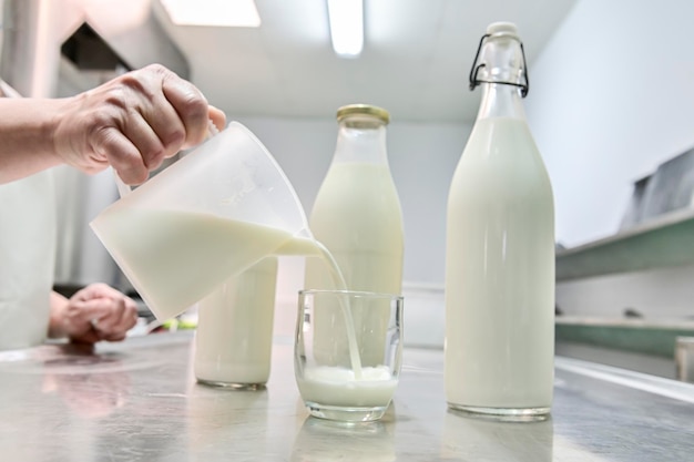 Verter leche de una jarra en un vaso en el fondo botellas de vidrio llenas