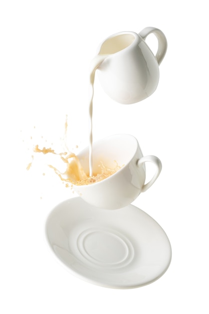 Verter la leche y salpicaduras de té con leche de taza y plato volador aislado sobre fondo blanco.
