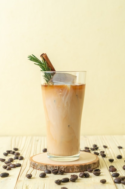 Verter la leche en un vaso de café negro con cubitos de hielo, canela y romero sobre fondo de madera